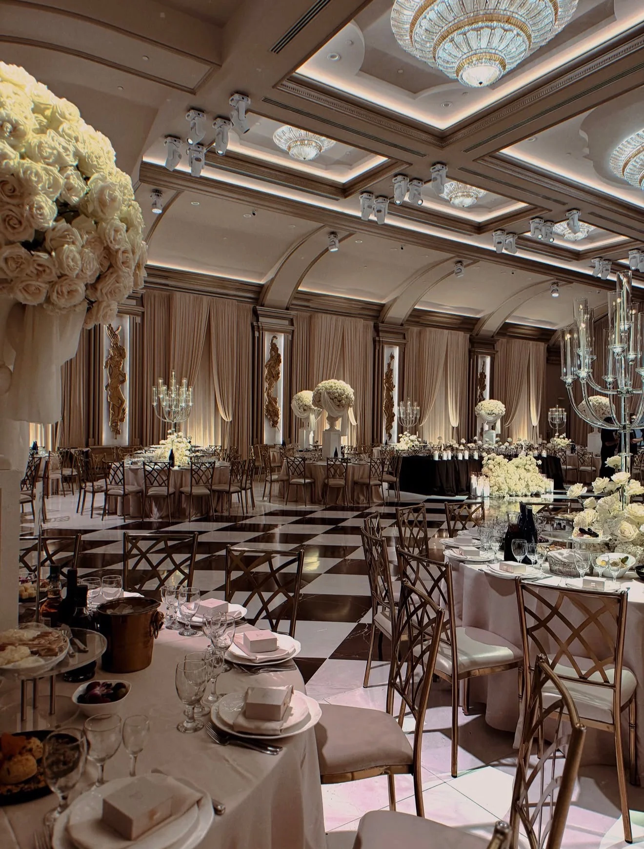 A large wedding ballroom with chandeliers, floral arrangements, and fully set tables