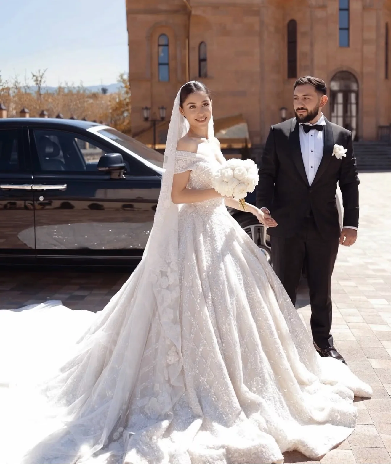 A bride and groom arriving for their wedding beside a luxury vehicle